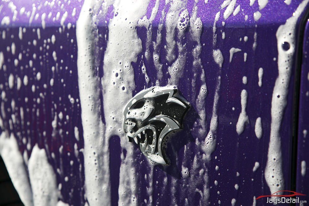 Purple car being washed, with a Hellcat emblem covered in soap suds.