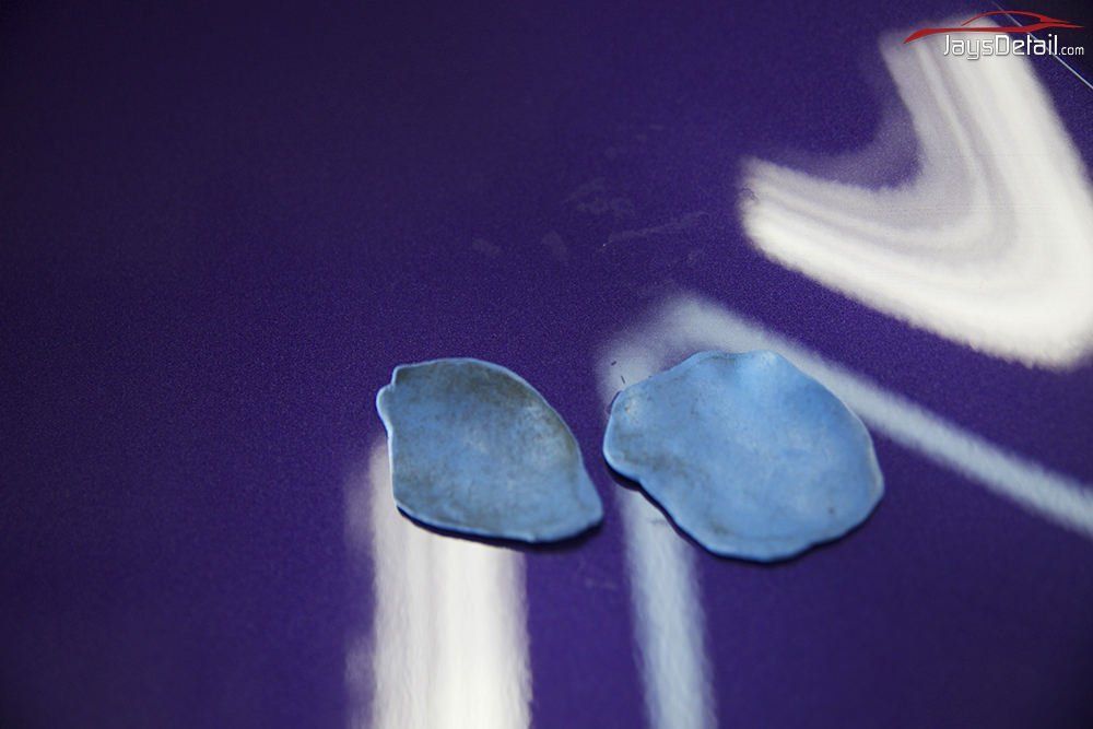 Two clay bar pieces on a purple car surface, likely for detailing. One is used, the other clean.