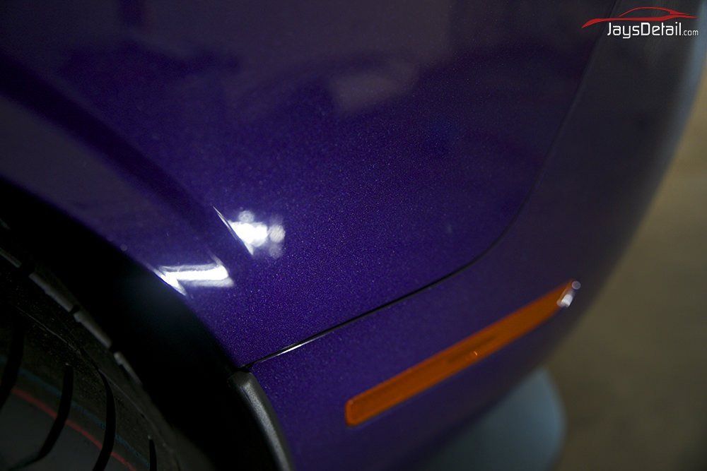 Close-up of a purple car fender with an orange side marker light and black tire.