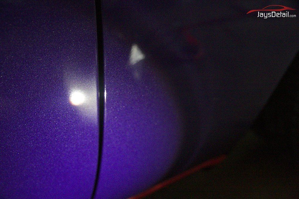 Close-up of a purple car door with metallic paint and a reflection of a light source.