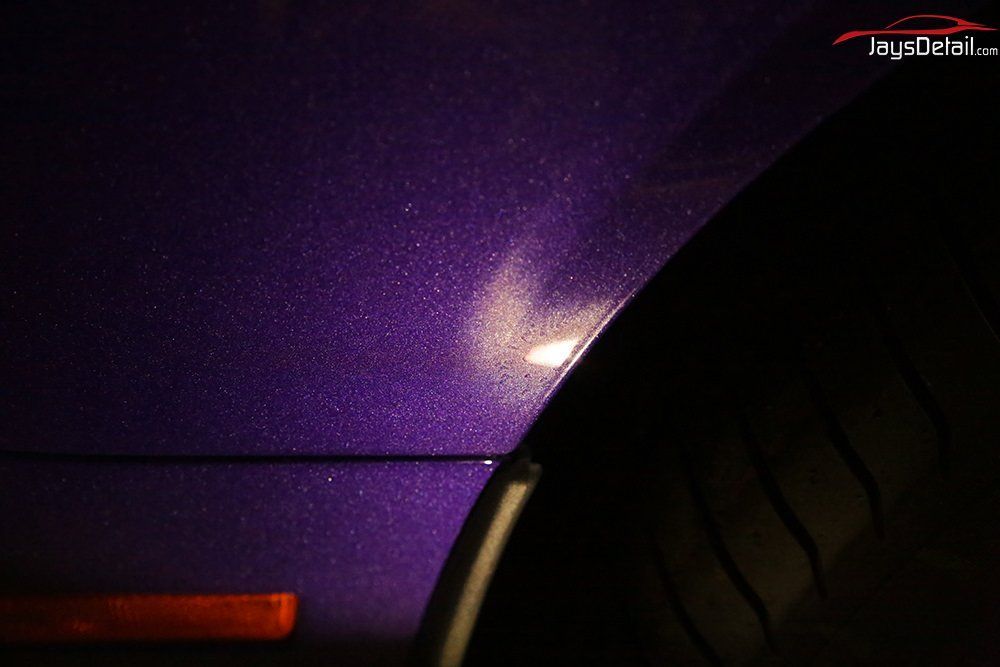 Close-up of a dark purple car with sparkling paint next to a black tire and orange reflector.