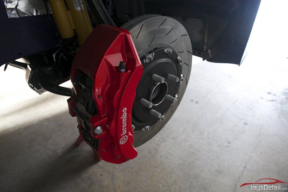 Red Brembo brake caliper and rotor installed on a car's front wheel.