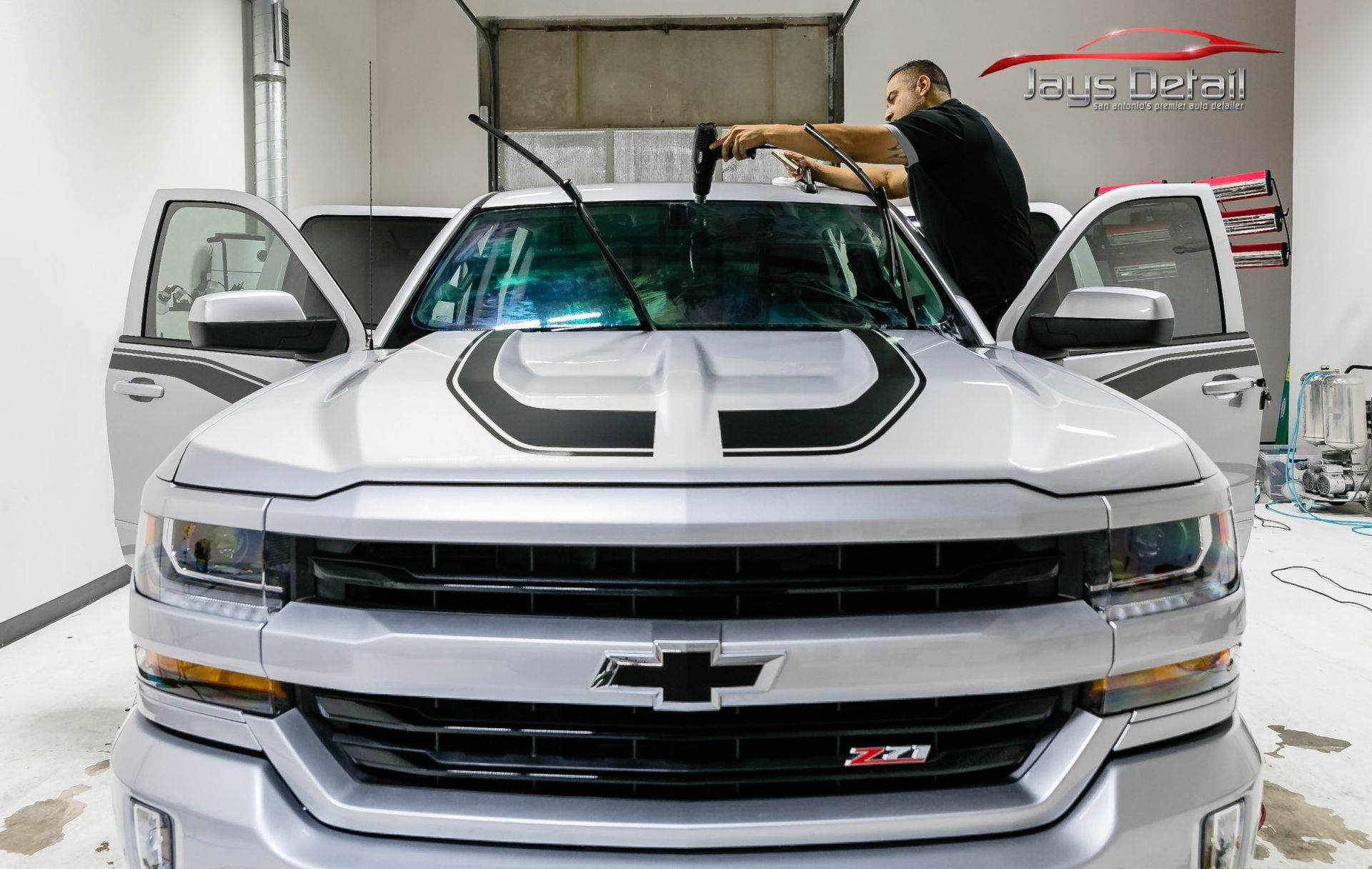 Silver Chevrolet pickup truck with window tinting being applied in a shop.