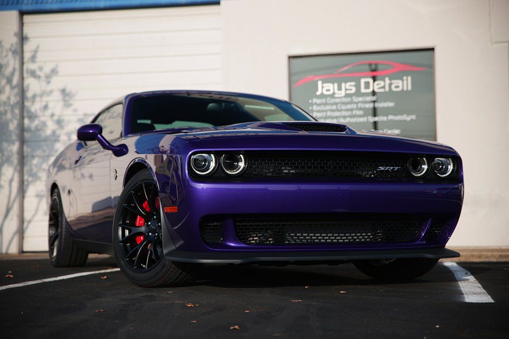 Purple Dodge Challenger parked in front of Jay's Detail shop. Red brake calipers, black wheels, and a bright exterior.