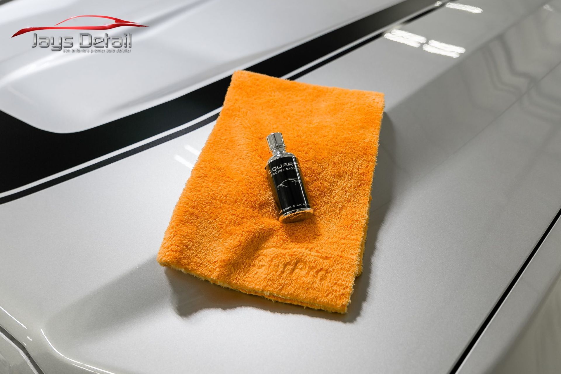 Orange microfiber towel and product on the hood of a car with black racing stripes.