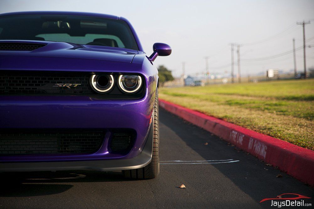 Purple Dodge Challenger parked on the edge of a road, close-up of the front with bright headlights.