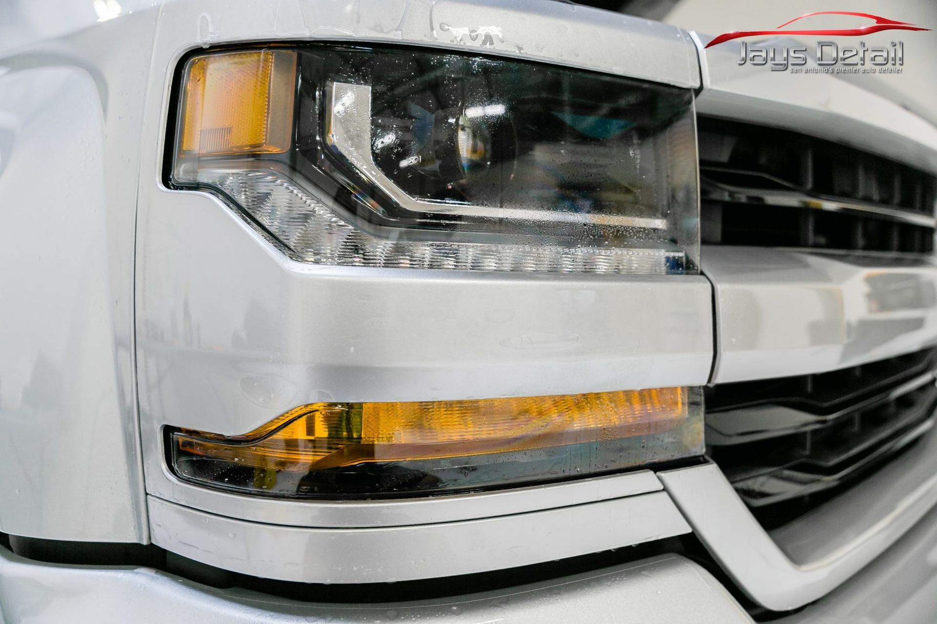 Silver truck front headlight and grille, close-up.
