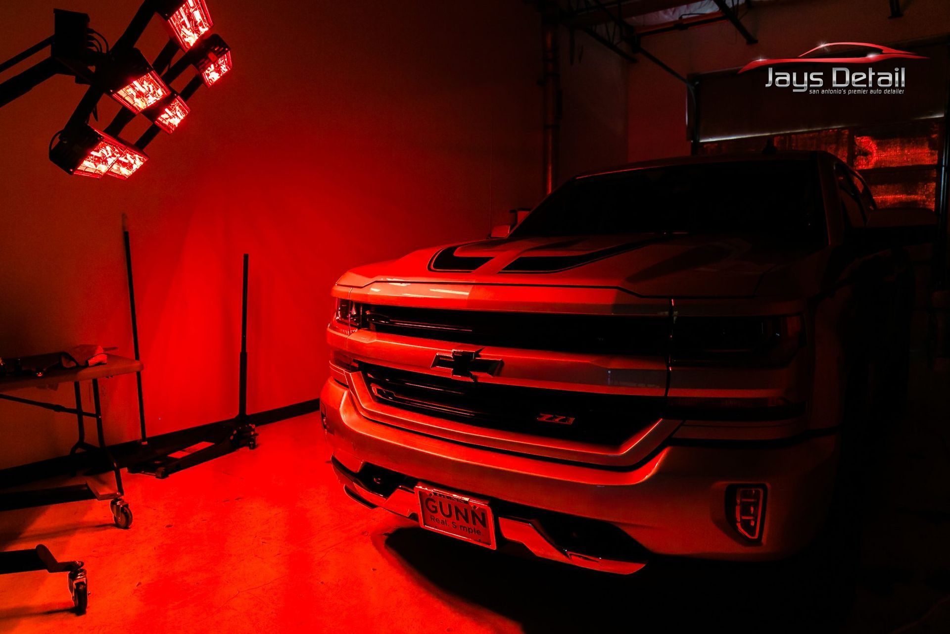 Red-lit Chevy truck inside a shop, illuminated by overhead detailing lights.
