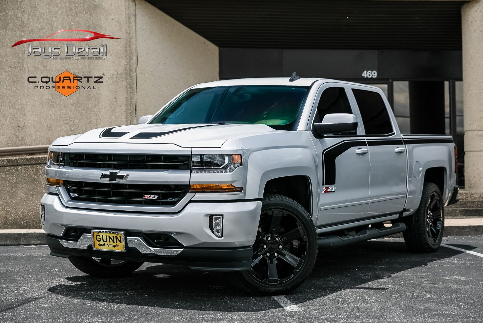 Silver Chevrolet pickup truck with black accents parked in front of a building.