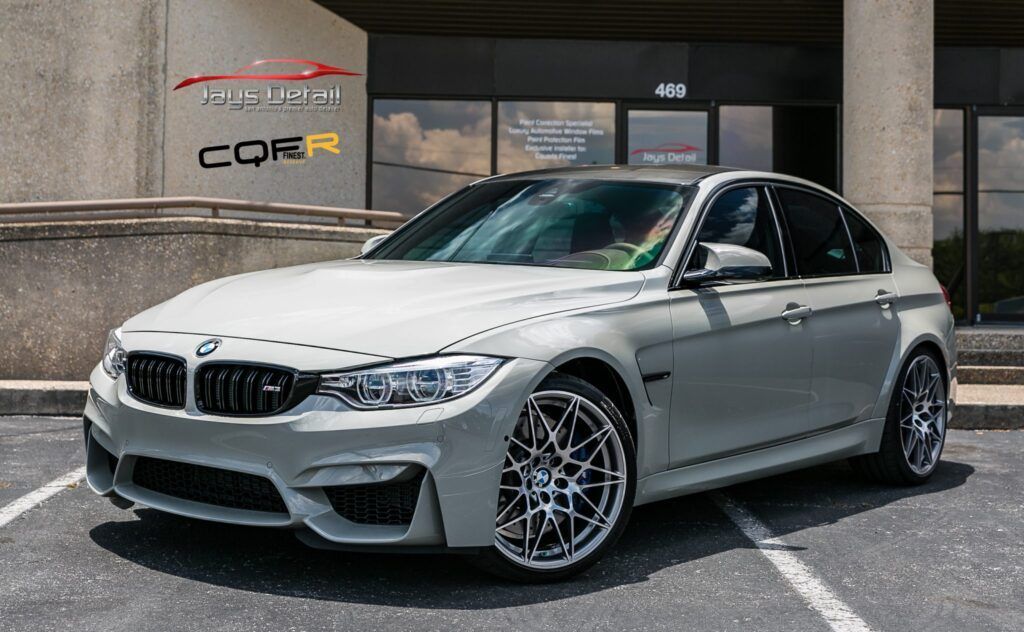 Gray BMW M3 sedan parked in front of a building with a business logo.