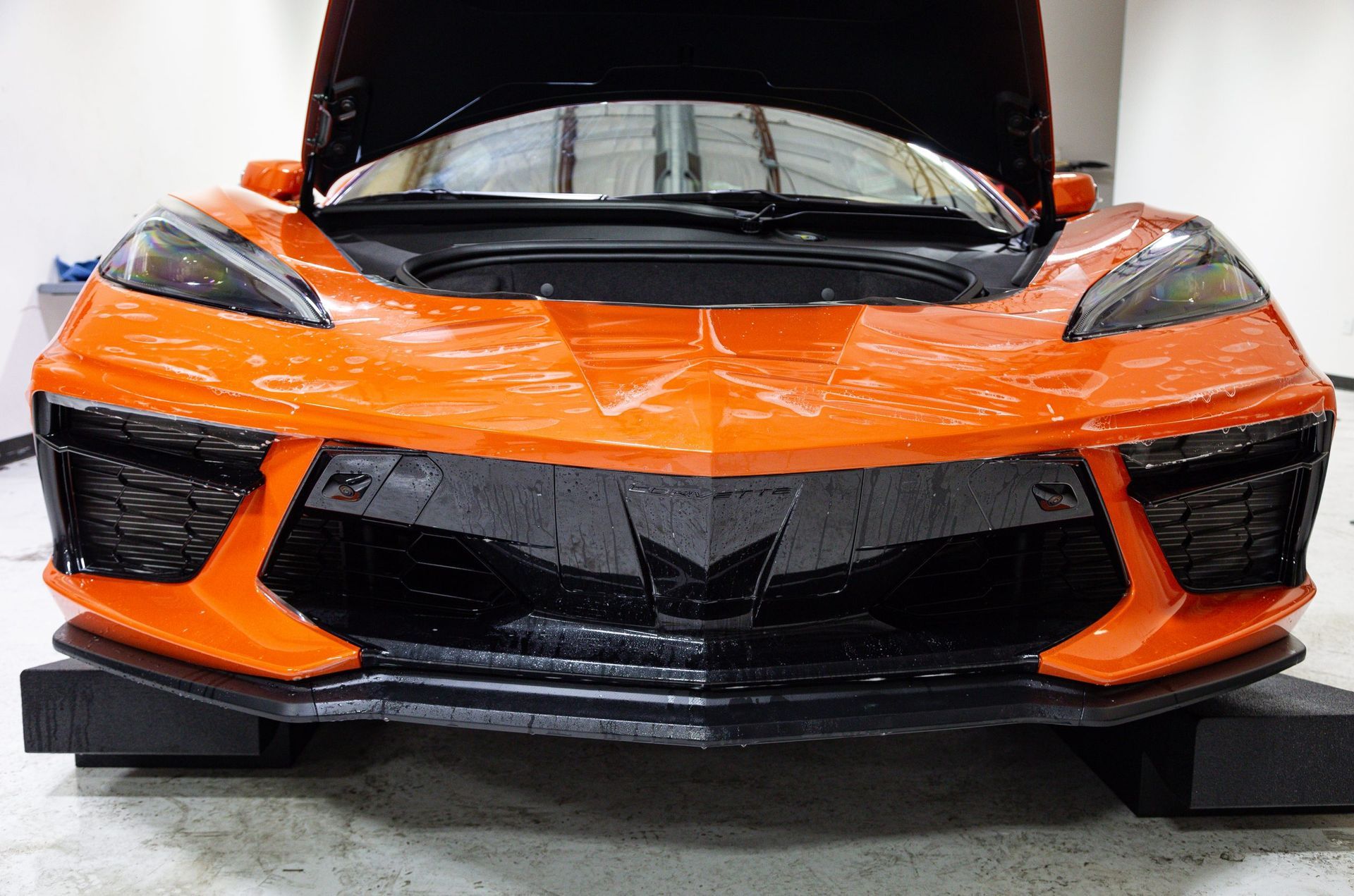 Orange and black sports car with open hood, front view.