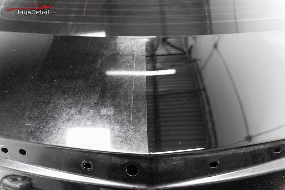 Black car trunk lid, half with swirls and scratches, other half polished and smooth.