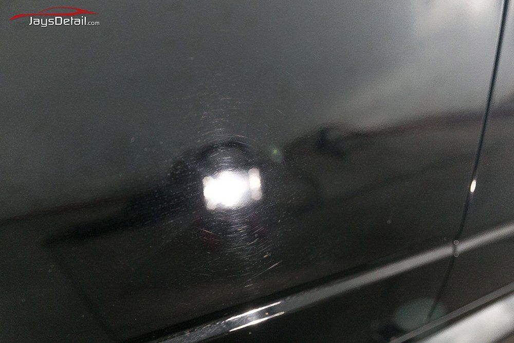 Black car paint with visible swirl marks reflecting a bright light.