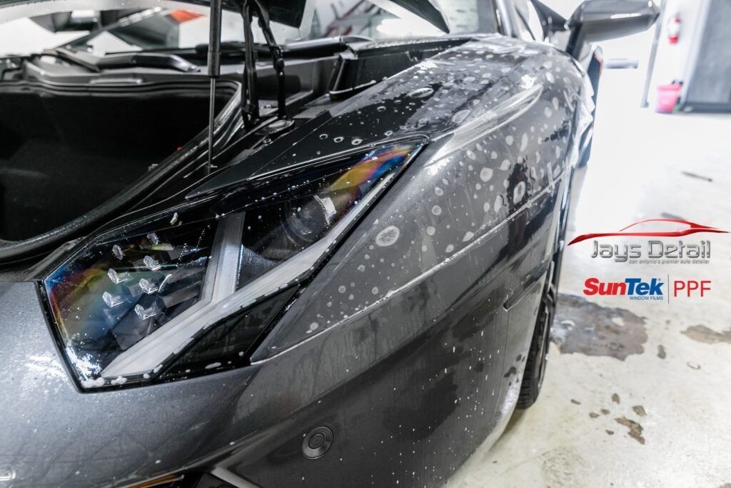 Black sports car getting paint protection film applied. Shiny surface with water droplets visible.