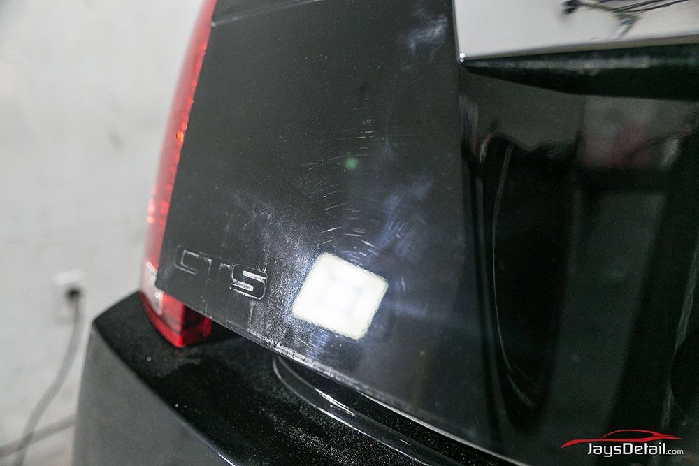 Black car trunk with scratches, a tail light, and a Crysler emblem, indoors.
