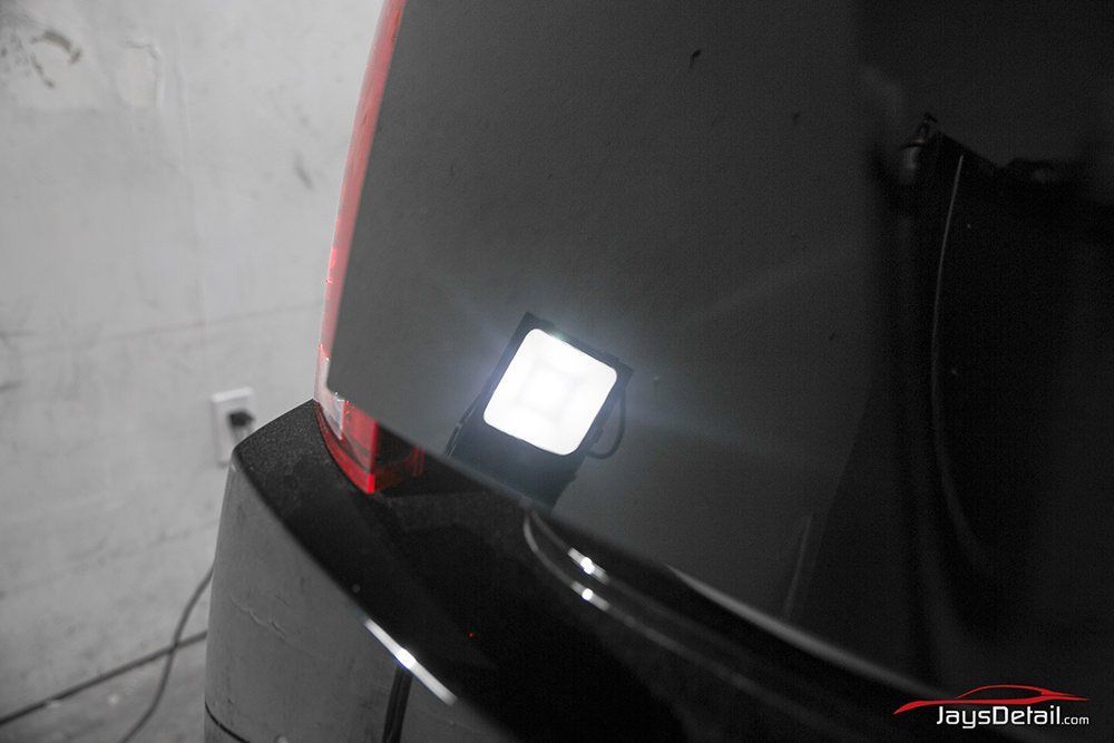 Black car body reflecting a bright white inspection light, revealing imperfections.