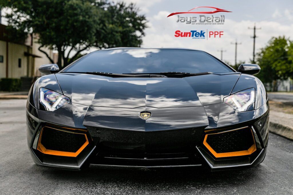 Black Lamborghini sports car with orange accents parked on a wet street.