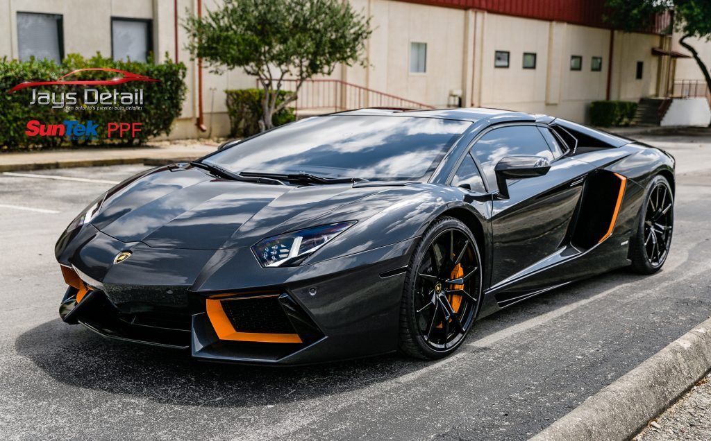 Black Lamborghini sports car with orange accents parked on a city street.