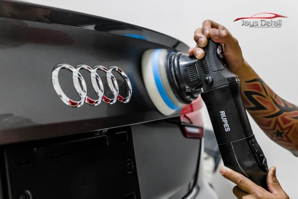 Person polishing a black Audi trunk with the logo visible.