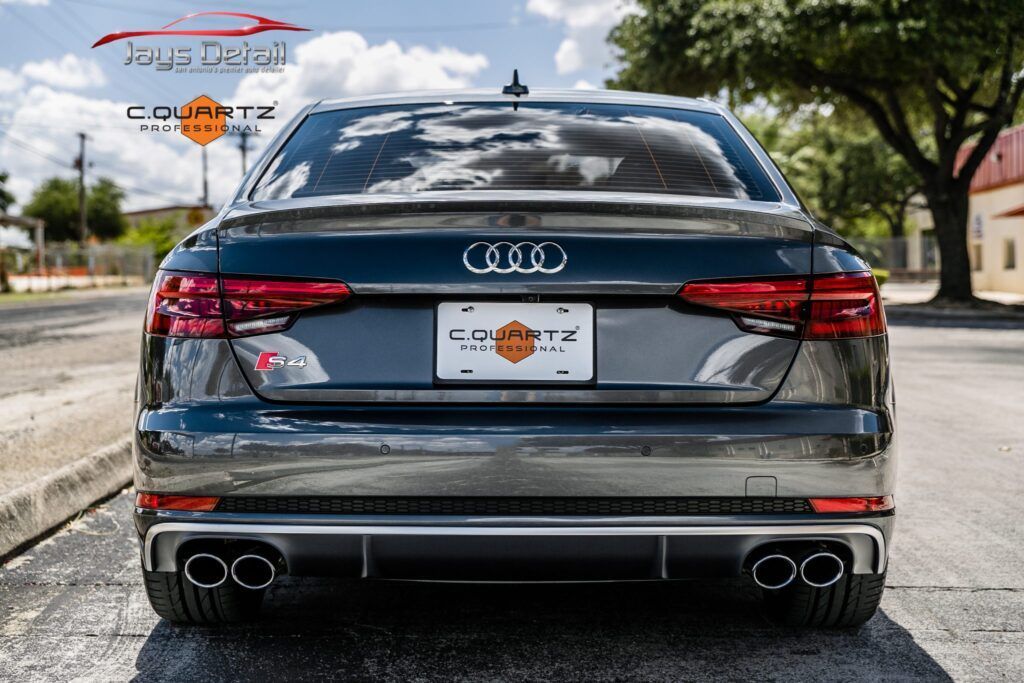 Gray Audi S4 sedan, rear view, with quad exhaust pipes, parked on a street.