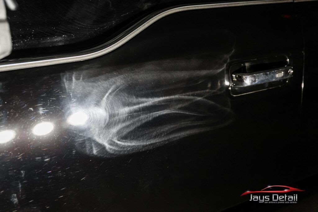 Swirl marks on a black car door near the handle, showing detailing work.