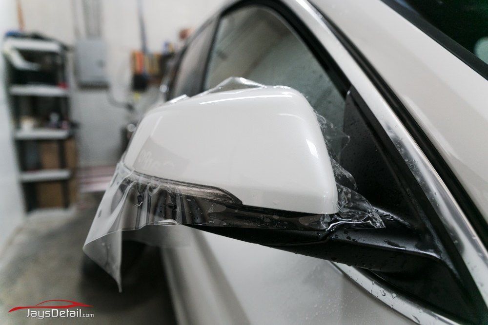 White car side mirror with protective film applied.