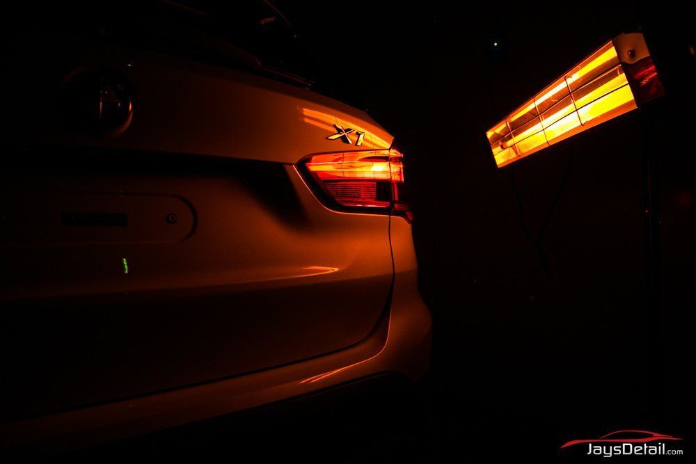 Car's rear illuminated by a bright orange heat lamp in the dark; close-up view.