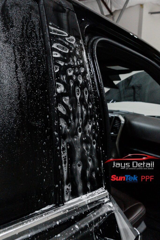Black car door being prepped with water and soap for paint protection film installation.