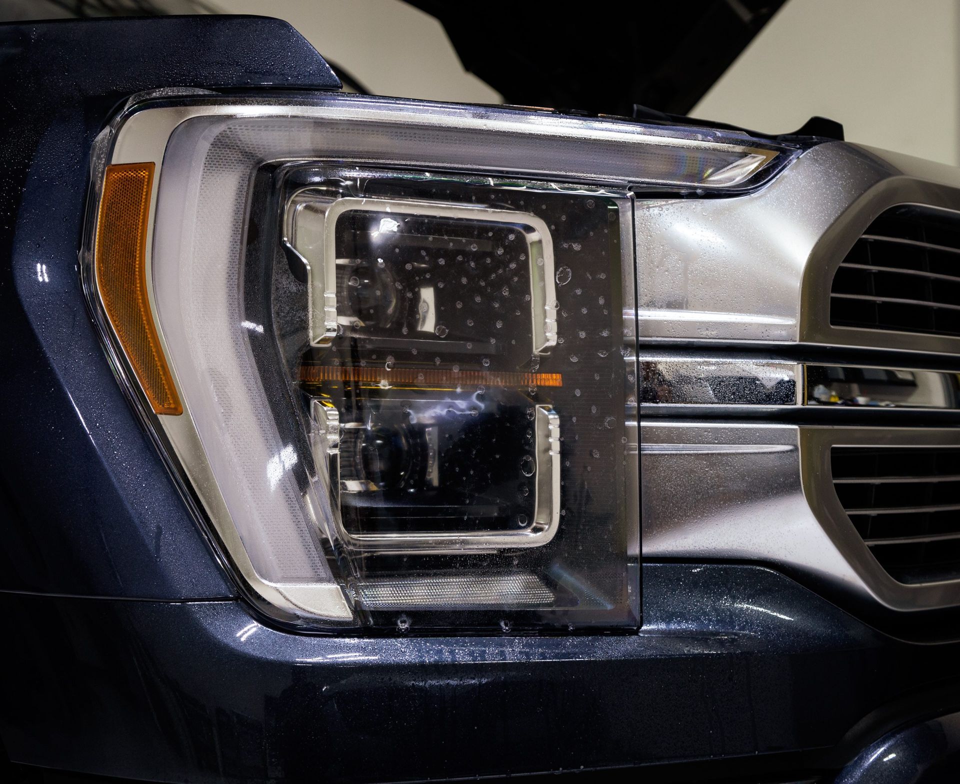 Close-up of a blue and silver truck headlight with water droplets on the surface.