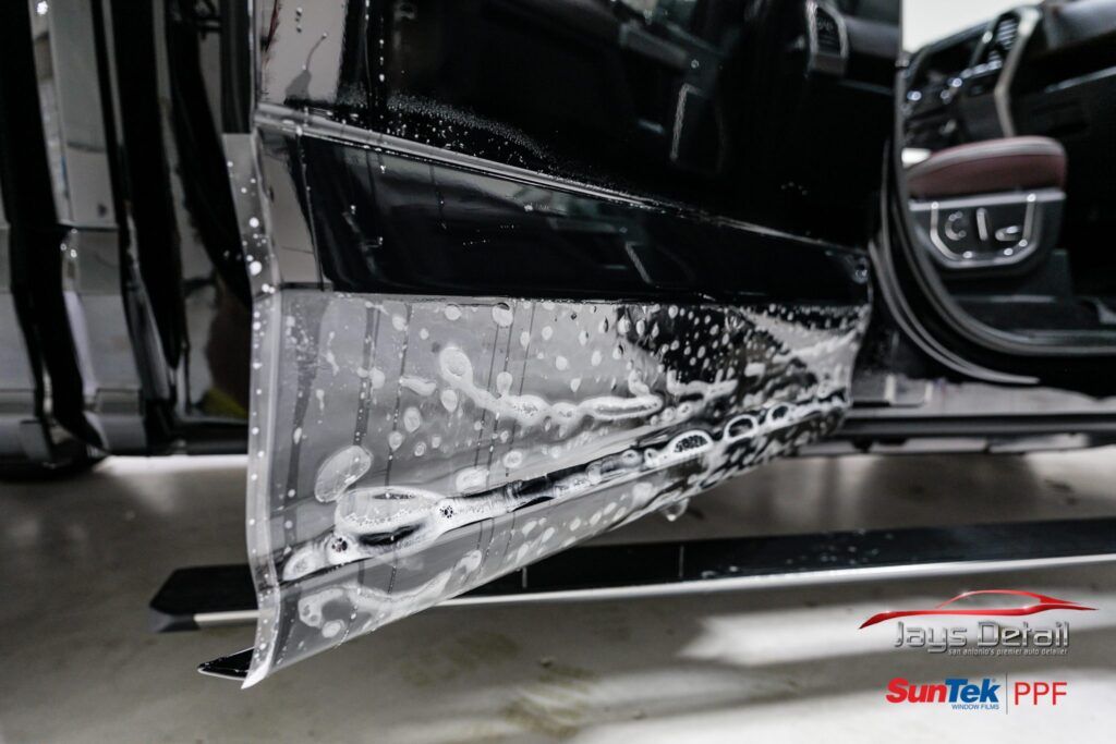 Car door with film being applied; black exterior, soapy water visible.