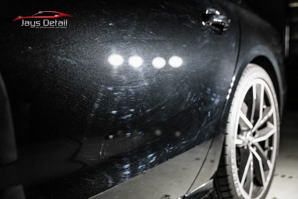 Black car door with visible swirl marks and light reflections.