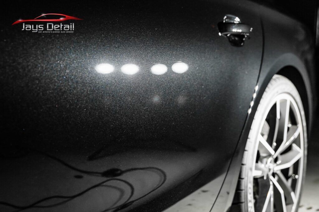 Black car door with reflections, close up. Shiny paint with light reflections, detailing work.