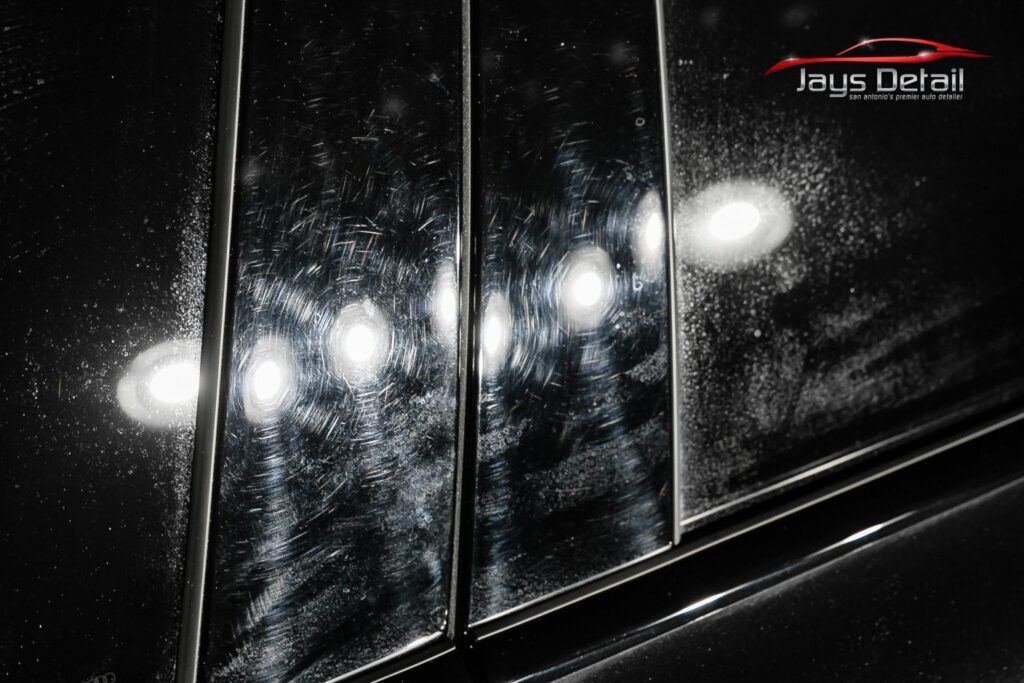 Black car's glossy pillar with swirls and reflections, reflecting light in a detailing setting.