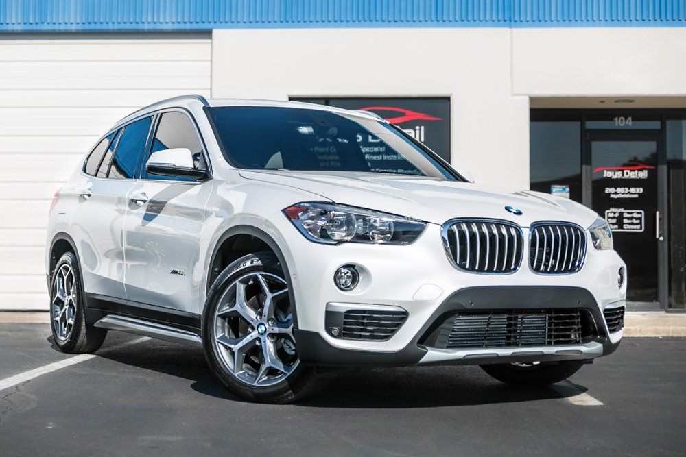 White BMW X1 SUV parked in front of a building with a blue awning.