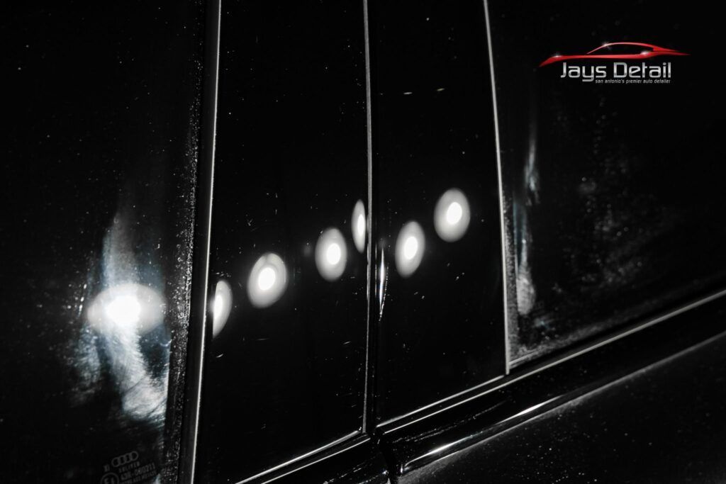 Close-up of a shiny, black car door reflecting bright lights.
