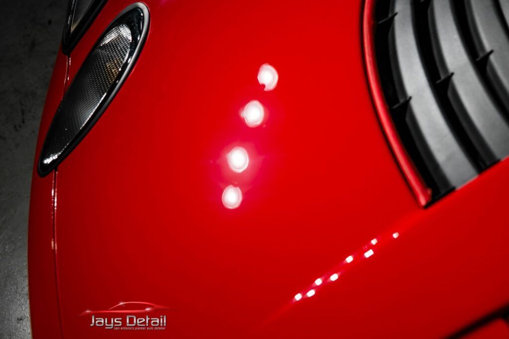 Red car's glossy paint with bright circular reflections. Side mirror and black vents are visible.