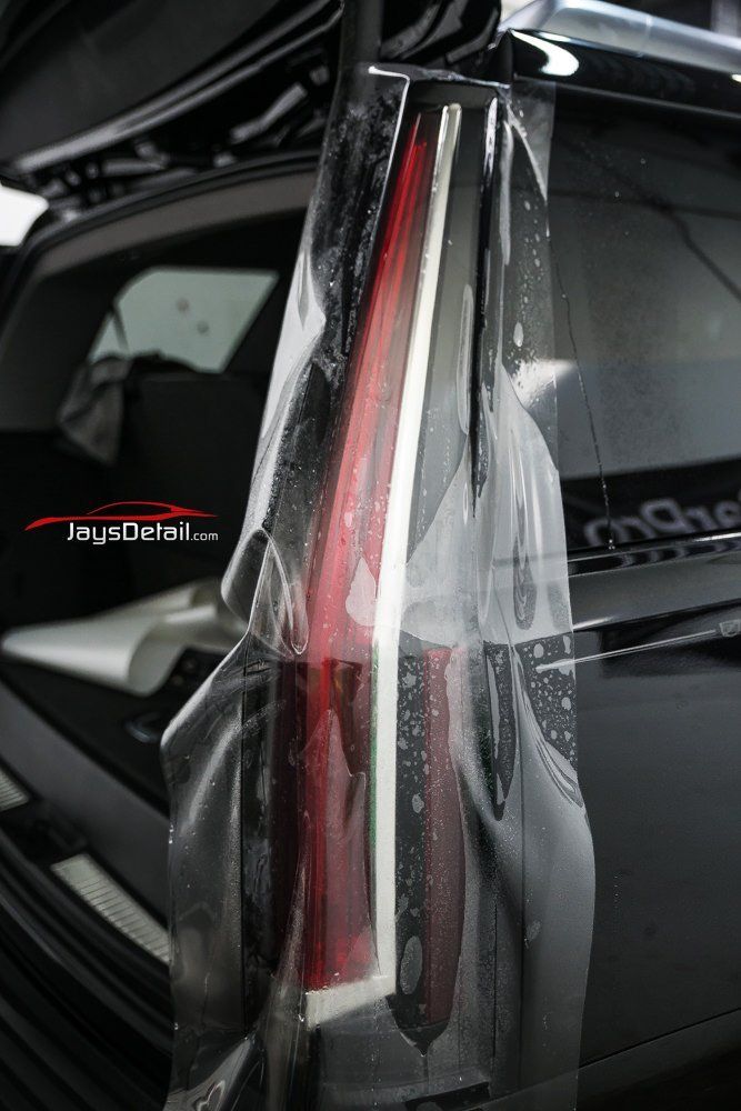 Clear protective film being applied to a black car's red taillight, showcasing the shape and detail.