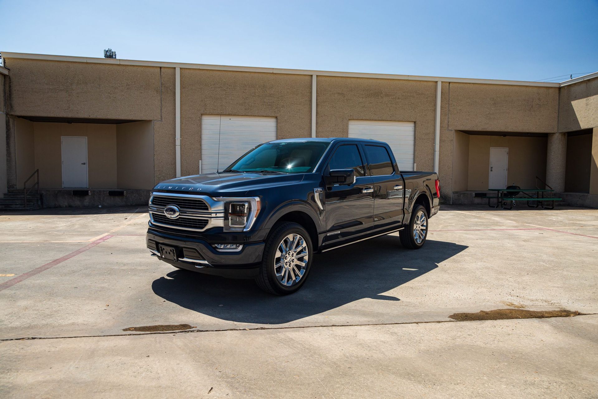 Dark blue Ford F-150 pickup truck parked outside a beige building on a sunny day.