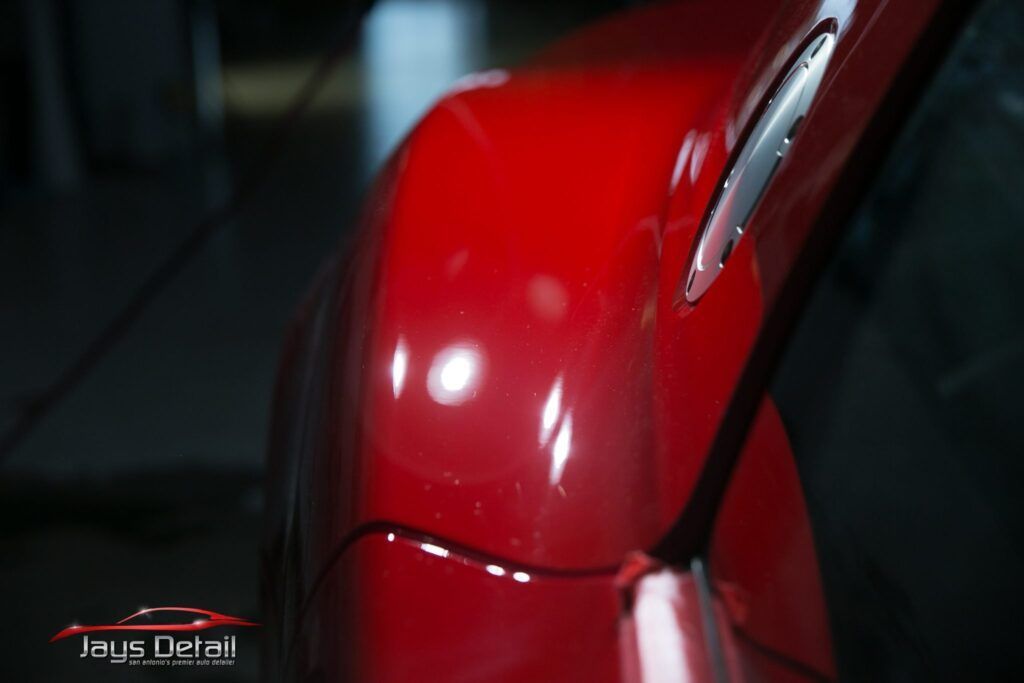 Red car fender with scratches, reflecting light.