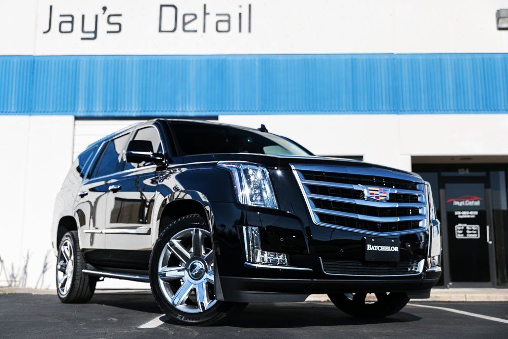 Black Cadillac SUV parked in front of Jay's Detail shop with blue and white exterior.