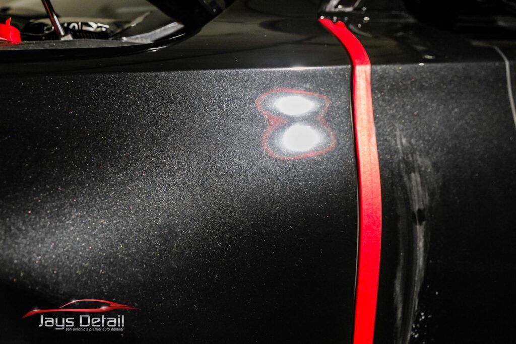 Black car panel with red tape, highlighting two polished spots.