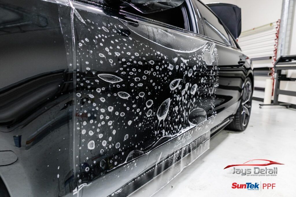 Black car with protective film applied, bubbles visible. Indoors, Jays Detail branding.