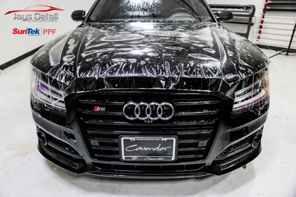 Black Audi being detailed with a clear protective film in a garage.