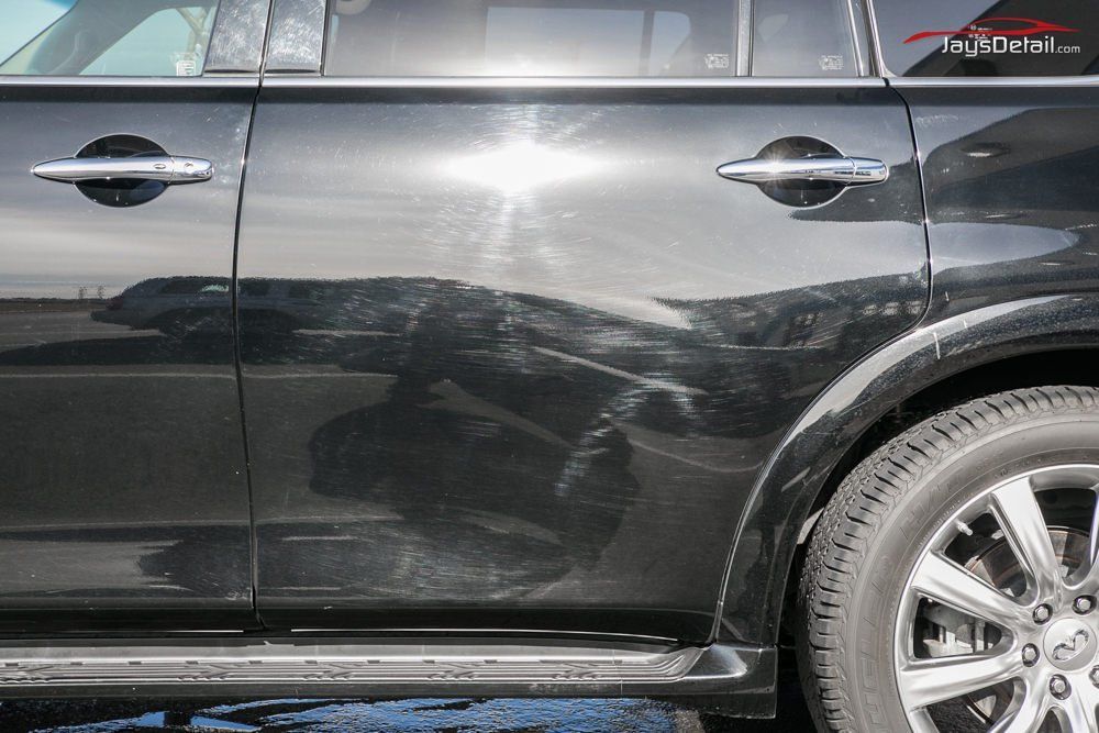 Black car with scratches on the side, chrome handles, and a wheel.