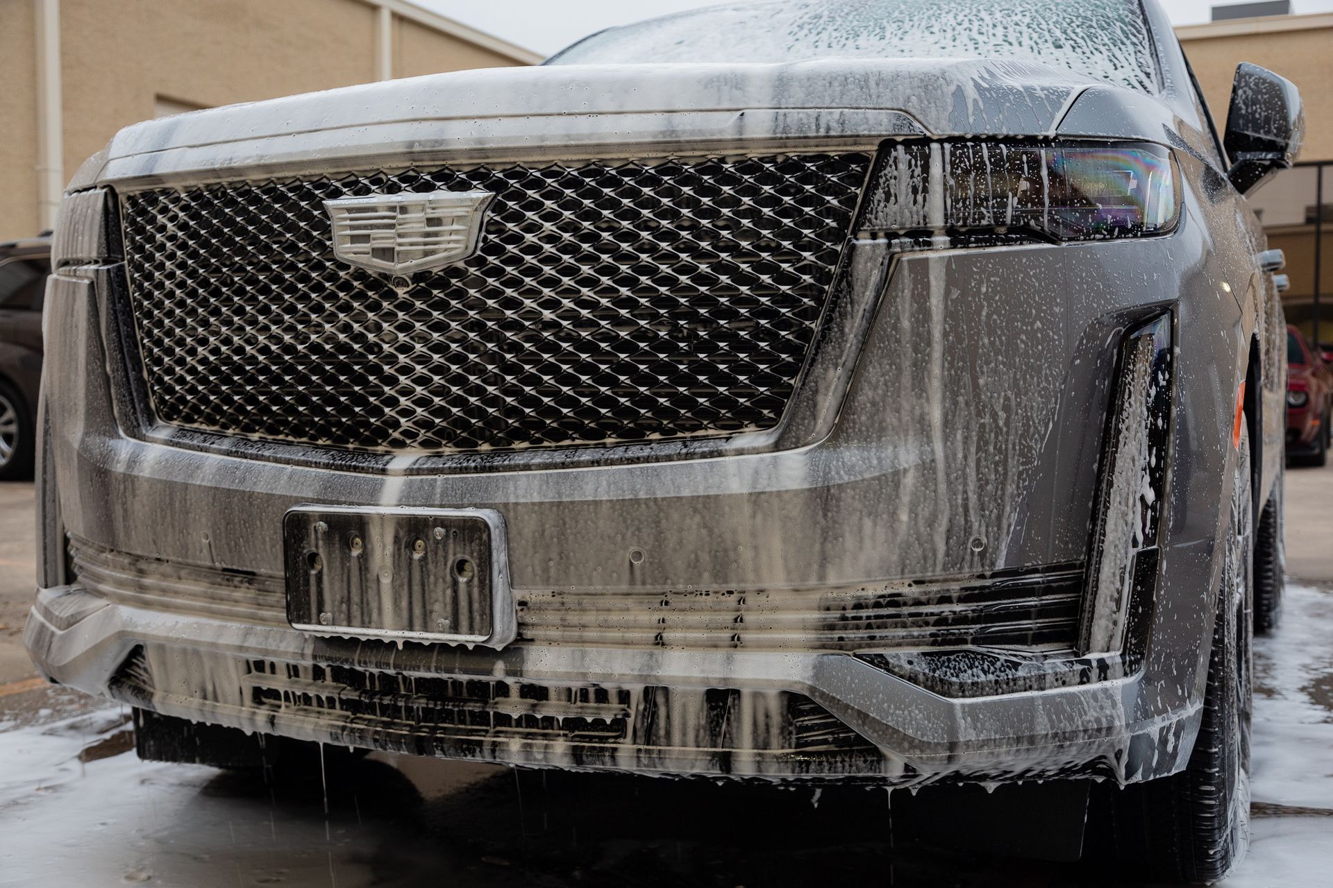 Cadillac SUV covered in white car wash foam; front view.
