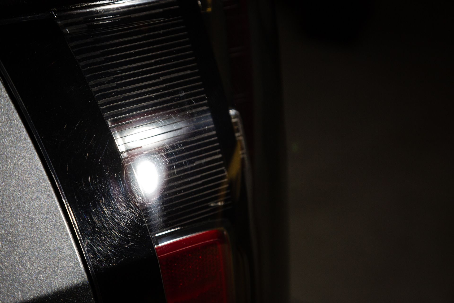 Close-up of a car's taillight. Black and silver with red accents, reflecting light.