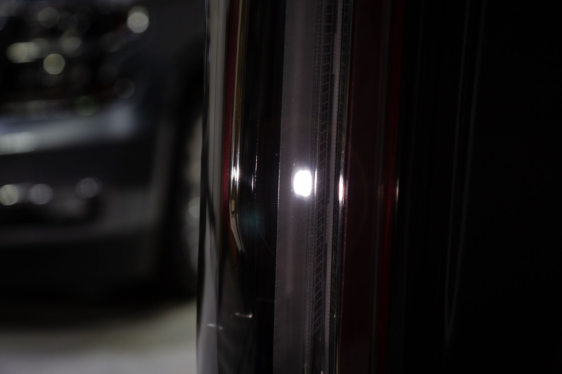Close-up of shiny black car parts reflecting light, with a blurry vehicle in the background.