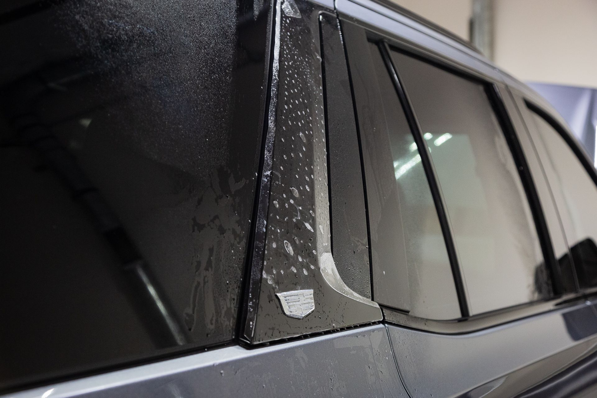 Close-up of a car's black window frame, with water droplets on the surface and peeling film.