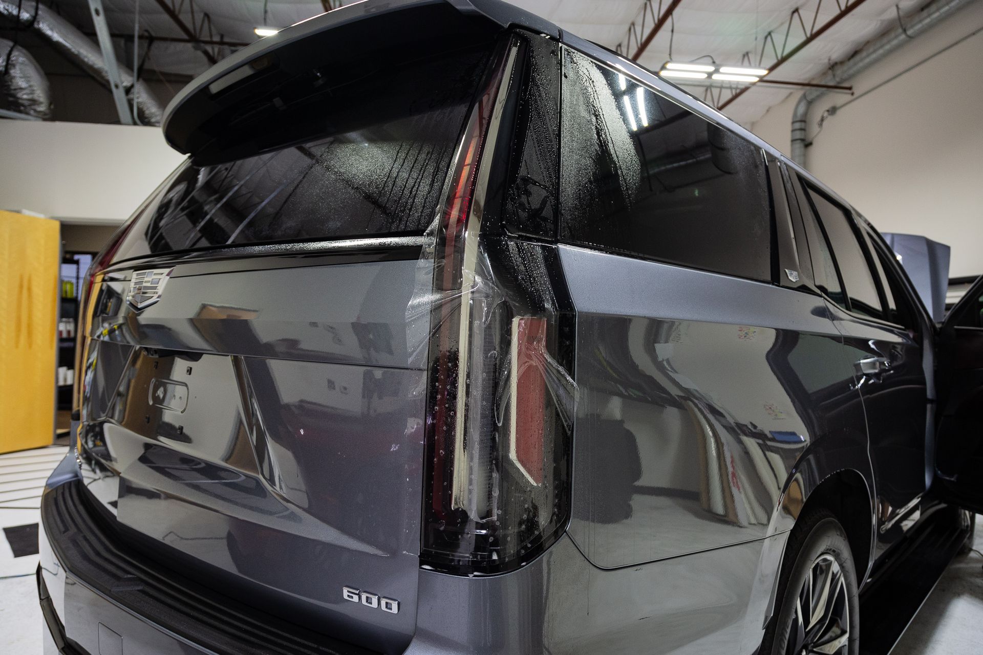 Rear view of a dark gray Cadillac SUV in a garage, showing tail lights and windows.