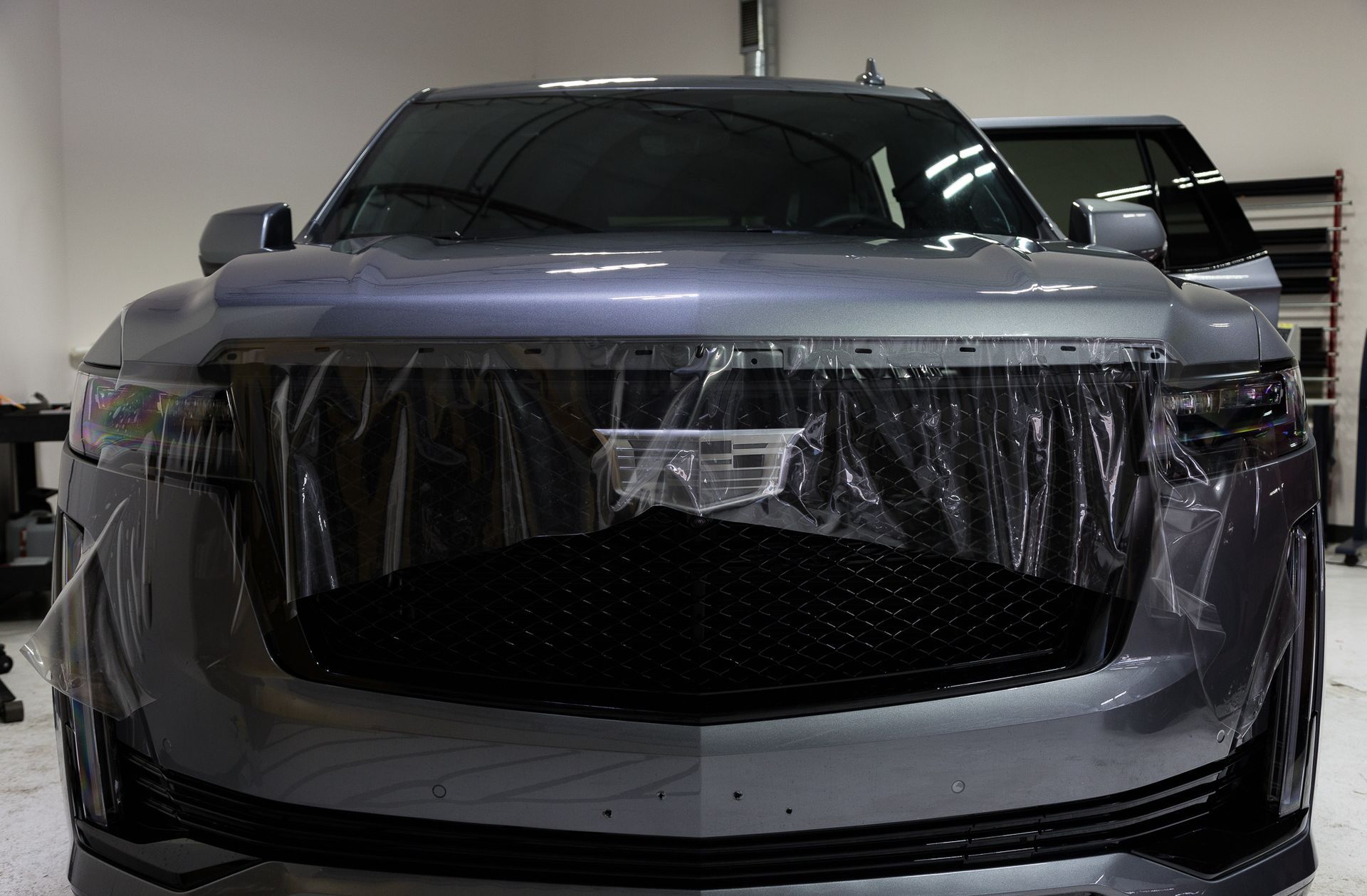 Gray SUV being wrapped in clear plastic in a shop.